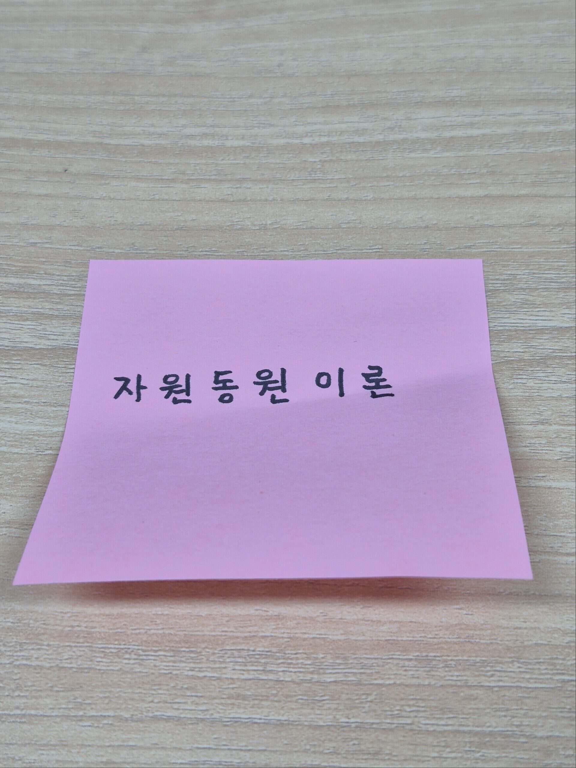 나무 책상 위에 '자원동원 이론'이라고 손글씨로 적힌 핑크색 포스트잇 메모지