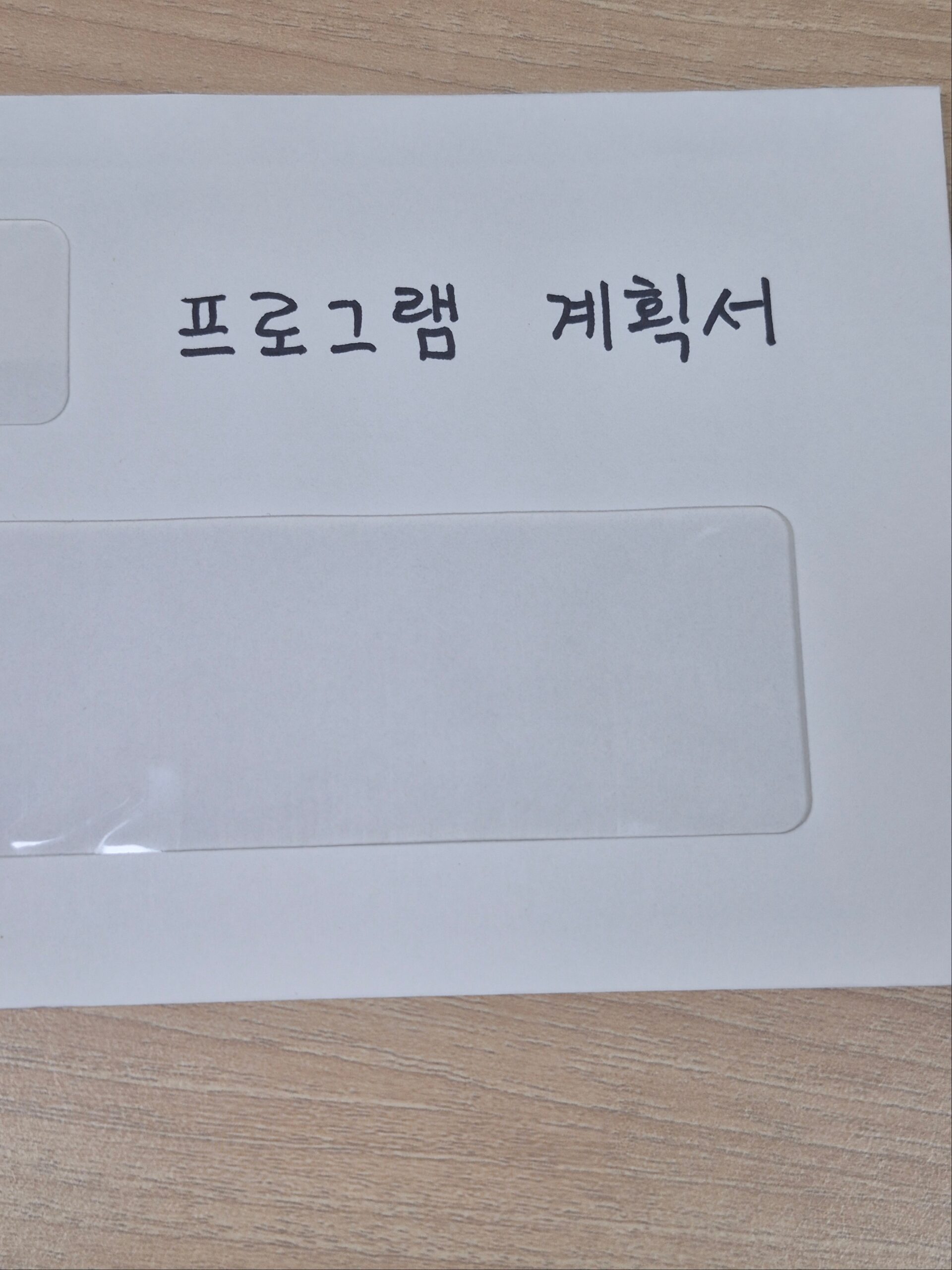 나무 바탕 위 서류 봉투에 손글씨로 프로그램 계획서라고 적힌 사진